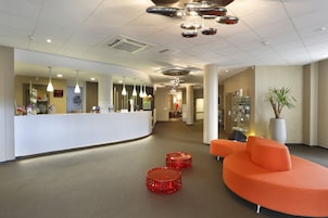 A modern reception area with a curved white counter, multiple pendant lights, and a seating area with orange sofas and red stools.