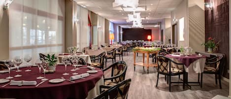A spacious dining area with round tables, chairs, and a stage in the background.