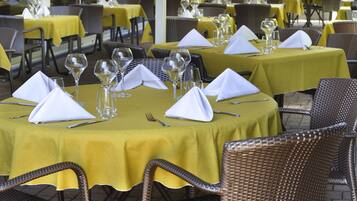 Un ristorante con tavoli apparecchiati per la cena, caratterizzato da tovaglie gialle e sedie in vimini.