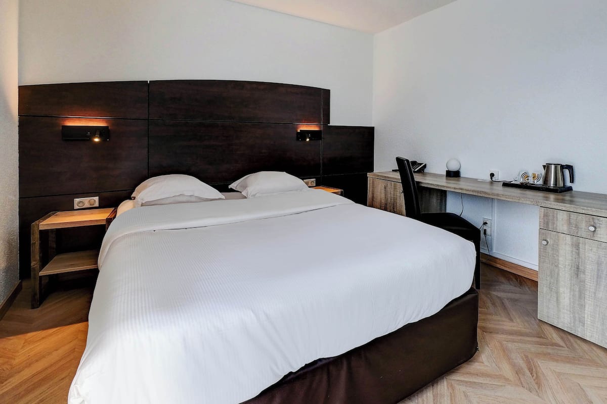 A modern hotel room with a large bed, bedside tables, a desk, and a chair.