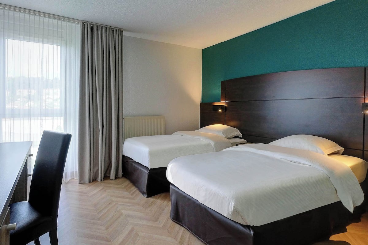 A hotel room with two beds, a desk, and a chair.
