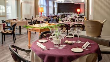 A restaurant with multiple tables set for dining, featuring a variety of table settings and a large champagne bucket.