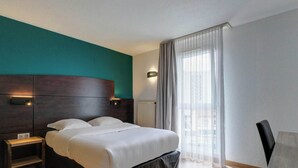 Ein Hotelzimmer mit einem großen Bett, einem Nachttisch, einem Stuhl und einem Fenster mit Vorhängen.