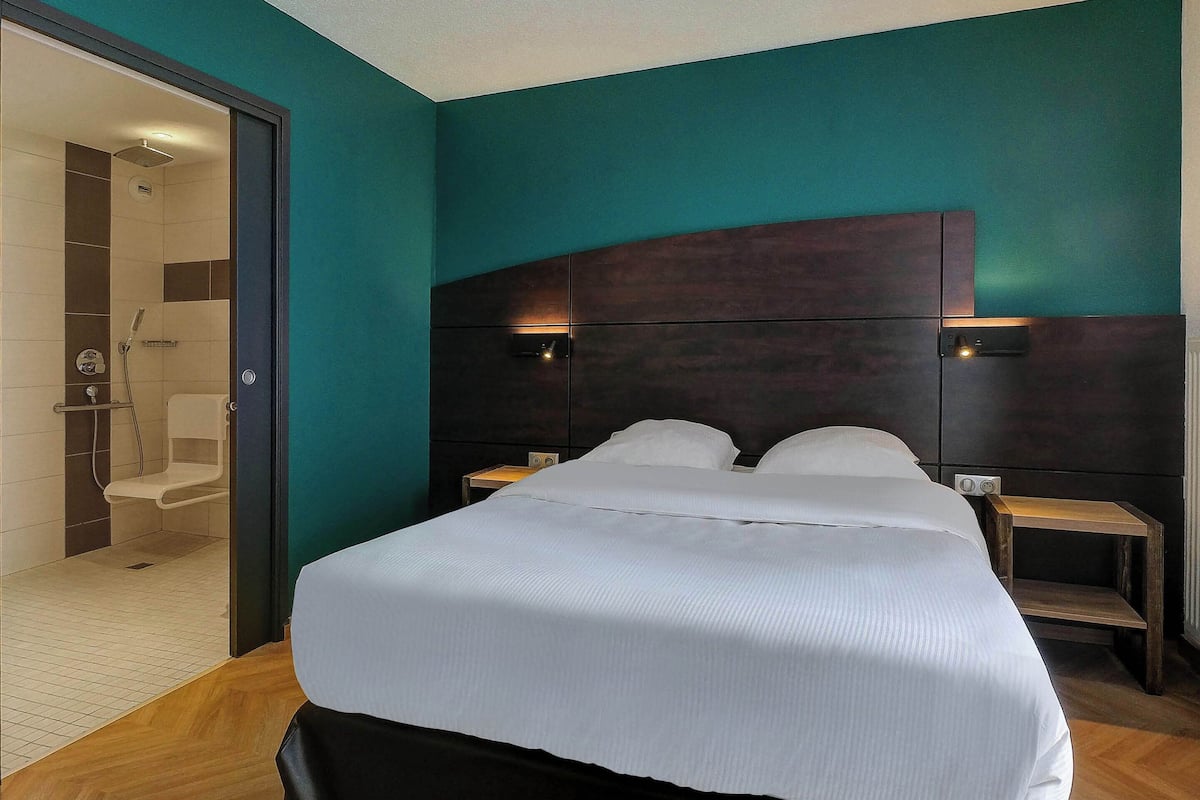 A modern hotel room with a large bed, a wooden headboard, and a separate shower area.