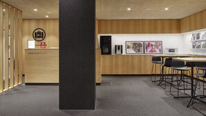 Un vestíbul d'hotel modern amb taulell de recepció, parets amb panells de fusta, un pilar negre i una zona de seients amb cadires negres.