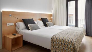 Habitación de hotel con una cama grande, una mesita de noche, una manta decorativa y vistas al exterior a través de una ventana con cortinas.