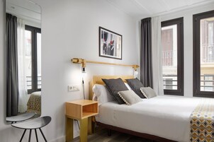 A hotel room with a bed, bedside table, chair, and a window with curtains.