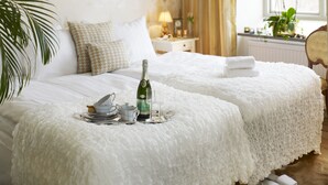 Una cama impecable con una botella de champán, una bandeja con tazas de té y un frutero con fruta.