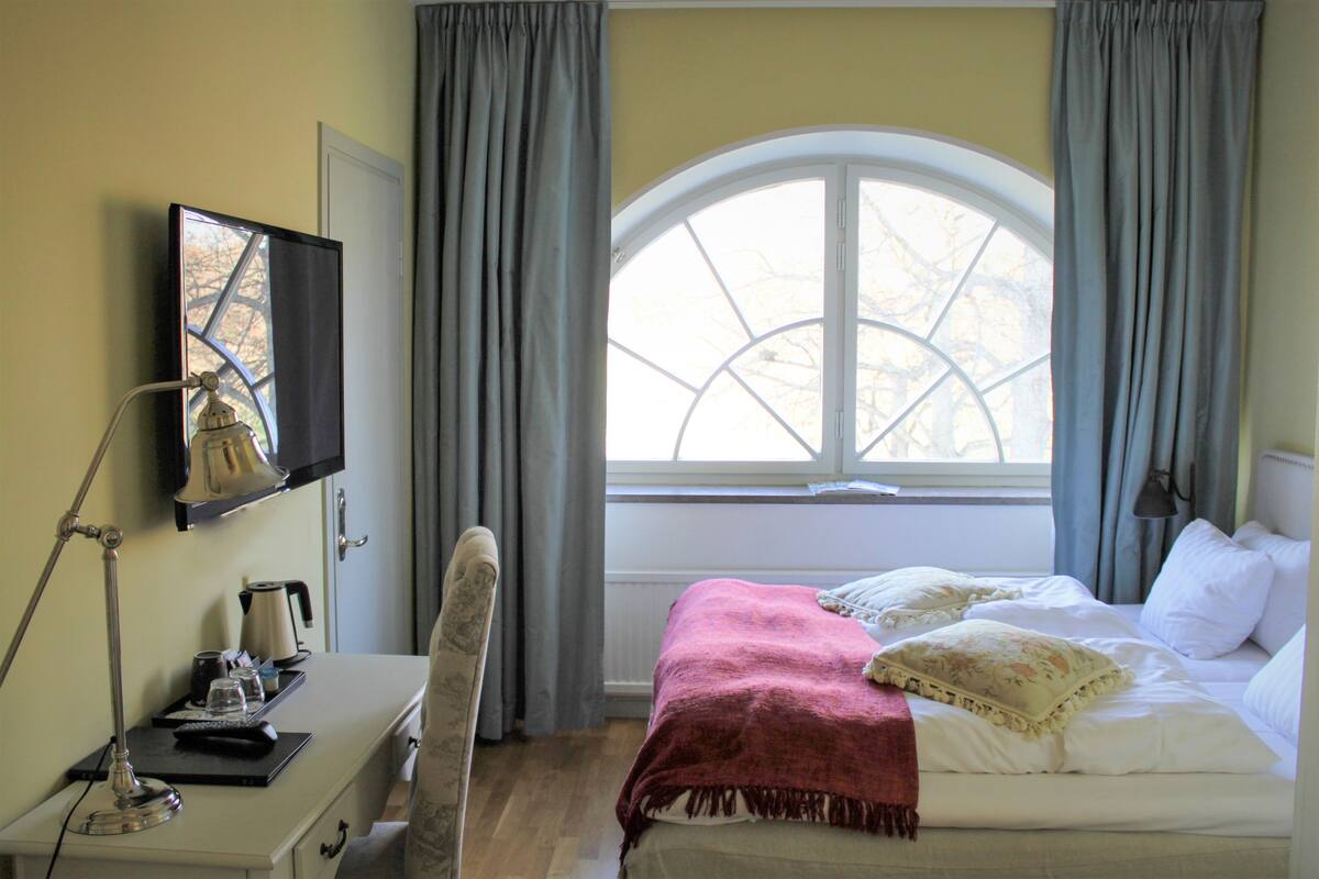 Habitació d'hotel amb llit, escriptori, cadira, televisió i finestra amb cortines.