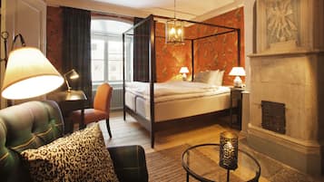 Una cama con dosel, una mesita de noche, un sillón con cojín estampado de leopardo, una mesa redonda con una vela y una chimenea.