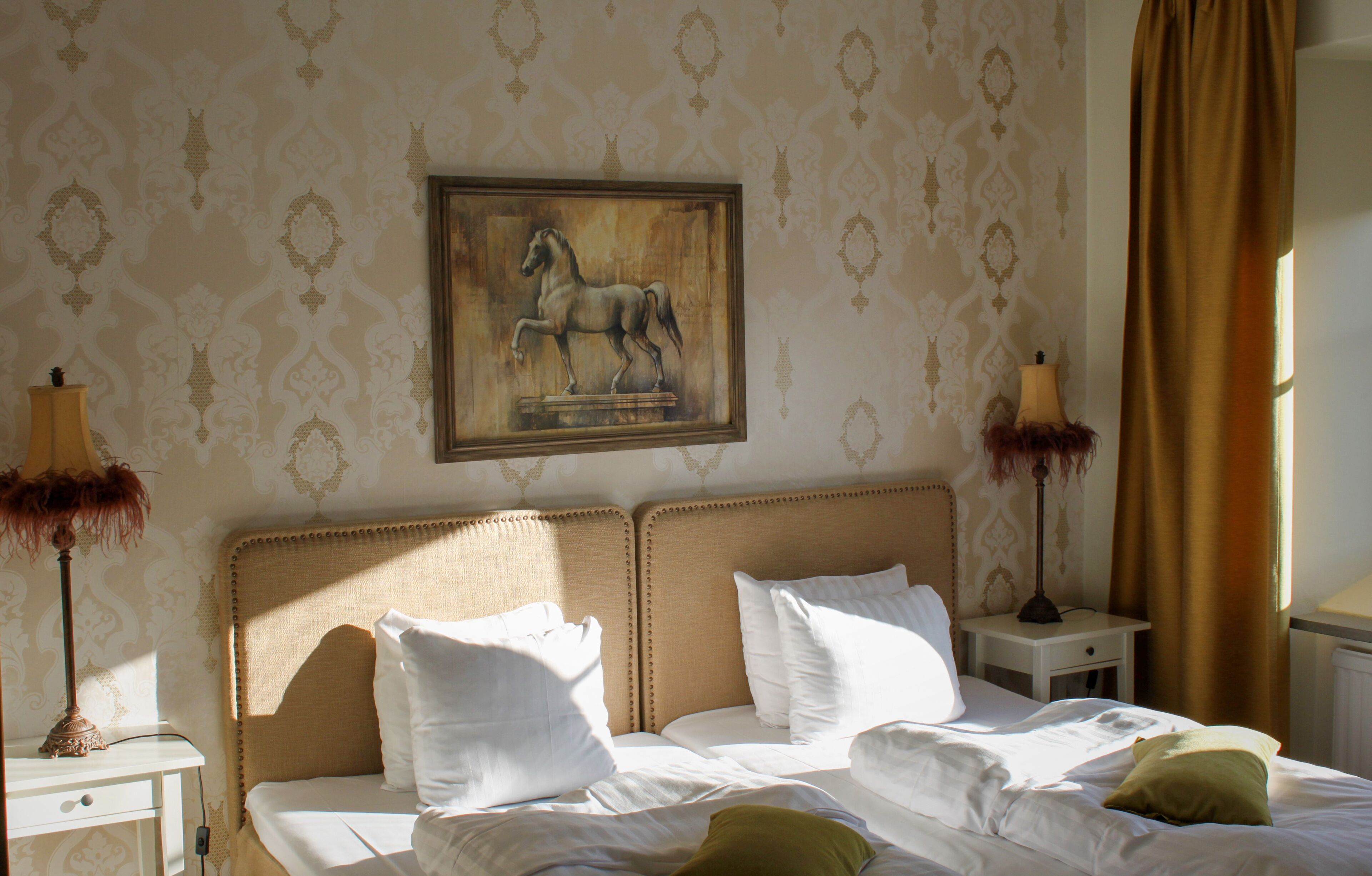 Une chambre d’hôtel avec un lit, deux tables de chevet, une lampe, un tableau représentant un cheval et un papier peint à motifs.