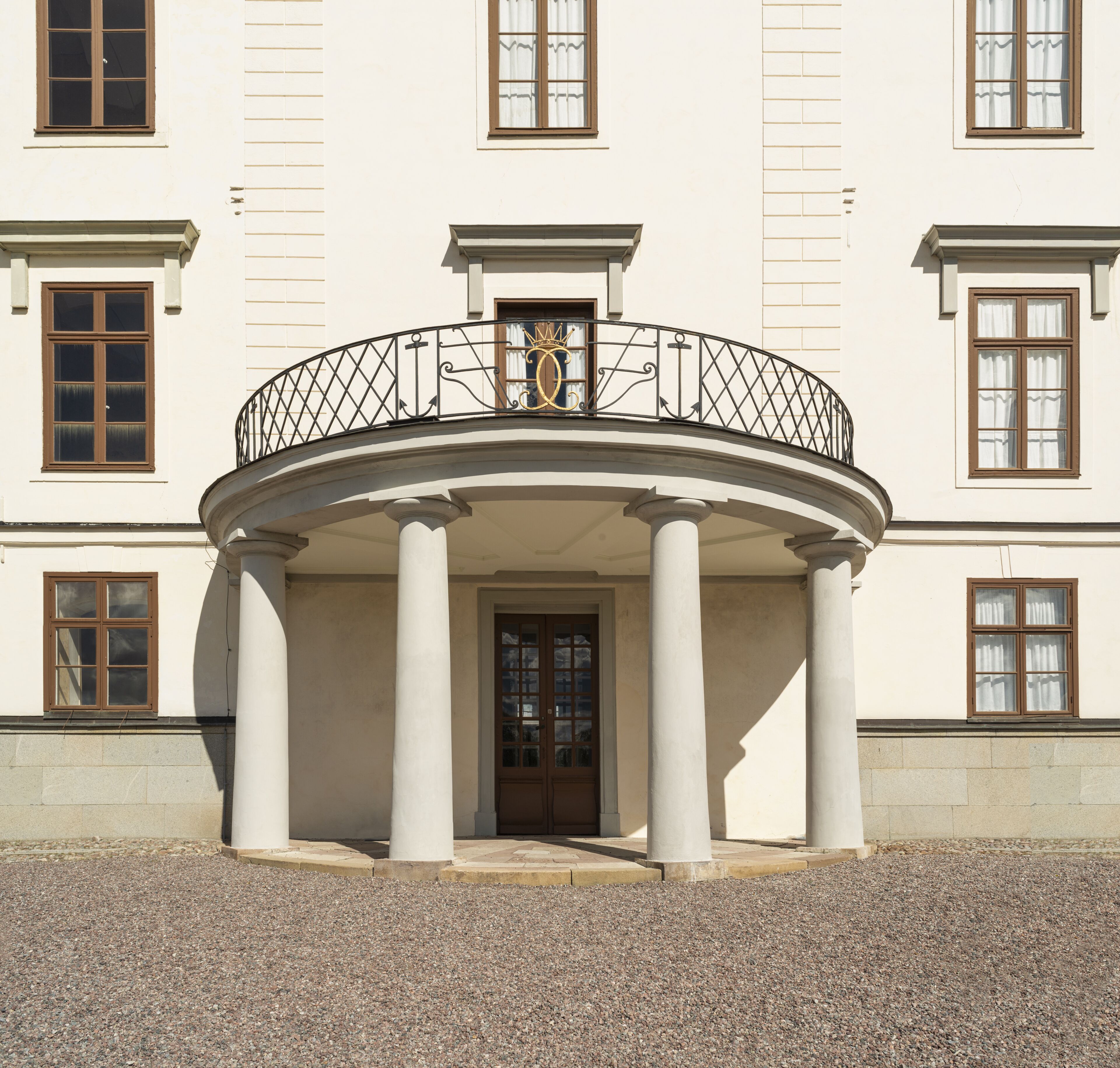 A building with a central entrance, flanked by columns, and a balcony with a railing.