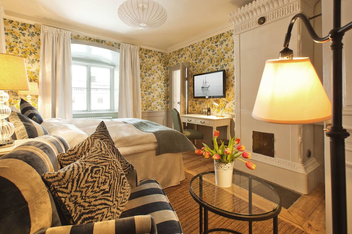Habitació d'hotel amb llit, escriptori, cadira, televisió, làmpada i un vas amb flors.