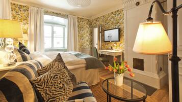 Une chambre d’hôtel avec un lit, un bureau, une chaise, une télévision, une lampe et un vase avec des fleurs.