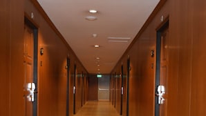 En lang, smal hotelgang med trædøre på begge sider, flisegulv og et loft med indbyggede spotlys.