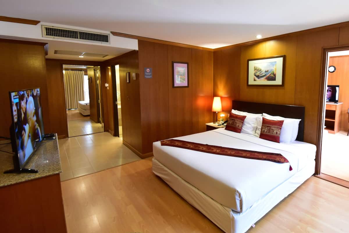 Une chambre d’hôtel avec un grand lit, une table de chevet avec une lampe, une télévision et une porte donnant sur un coin repas.