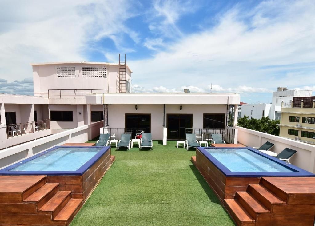 A rooftop with two swimming pools, a green lawn, and a building with a flat roof and windows.
