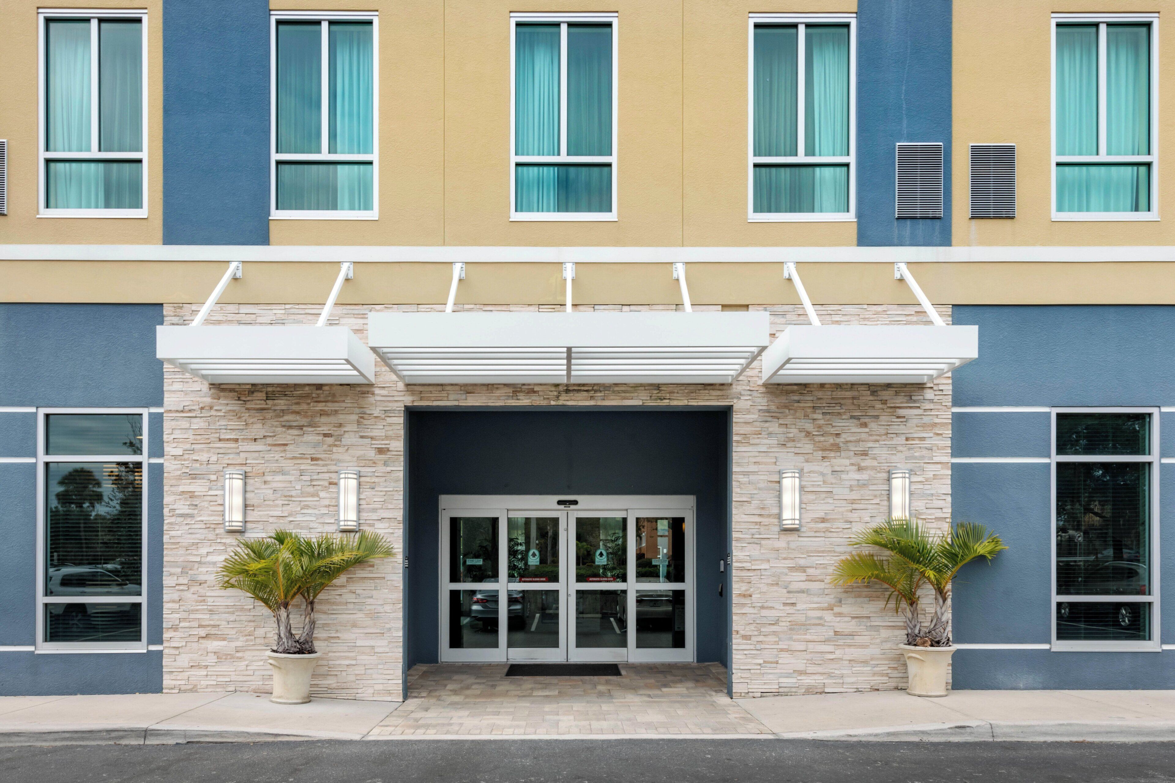 A building entrance with a glass door, stone facade, and two potted plants.