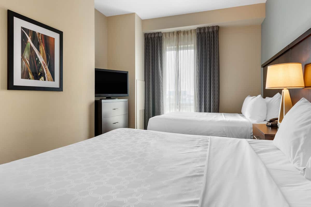 A hotel room with two beds, a television, a desk, and a window with curtains.