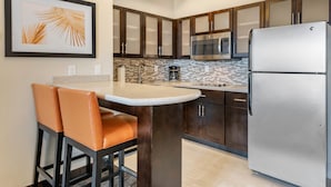 Una cocina moderna con armarios de madera oscura, un refrigerador de acero inoxidable, un microondas y un salpicadero de azulejos.