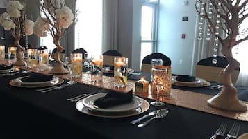 A long dining table set with plates, cutlery, and candles, flanked by decorative vases and a tree-like centerpiece.