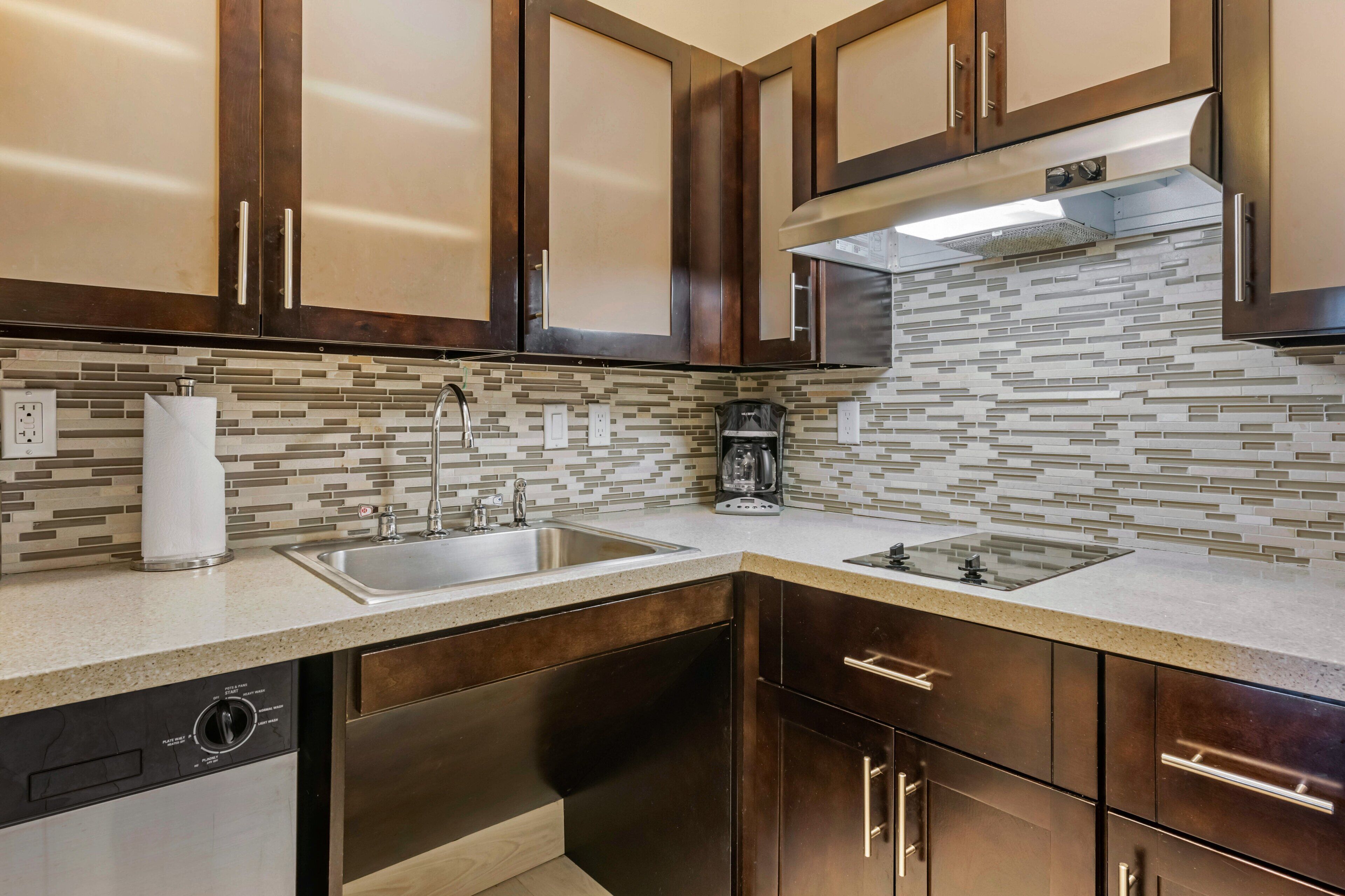 A modern kitchen with dark wooden cabinets, a stainless steel range hood, and a tiled backsplash.