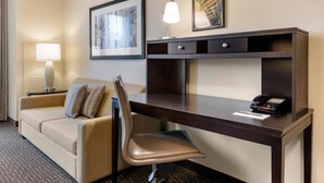 Habitación de hotel con sofá, escritorio con teléfono, silla, lámpara y cuadros en la pared.