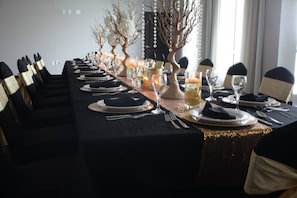 A long dining table set for a formal meal with multiple place settings, glasses, and a decorative centerpiece.