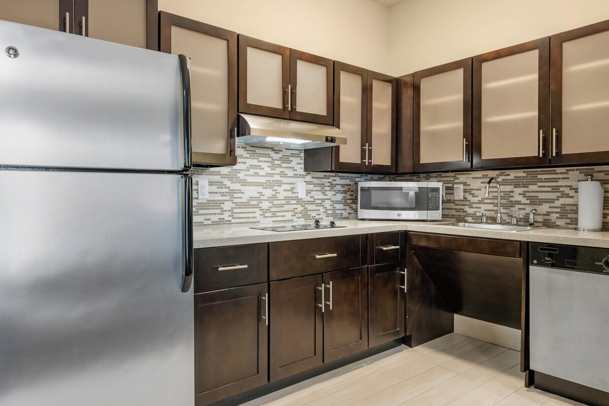 A modern kitchen with stainless steel appliances, dark wooden cabinets, and a tiled backsplash.