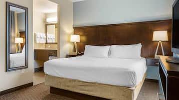 Habitació d'hotel amb un llit gran, un capçal de llit de fusta, un mirall, una tauleta de nit i un escriptori amb una làmpada.
