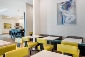 A modern dining area with yellow and blue chairs, white tables, and a large abstract painting on the wall. - Staybridge Suites St. Petersburg Downtown by IHG (St. Petersburg)