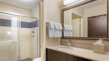A bathroom with a glass shower enclosure, a white toilet, a sink with a mirror above it, and a towel rack with towels.