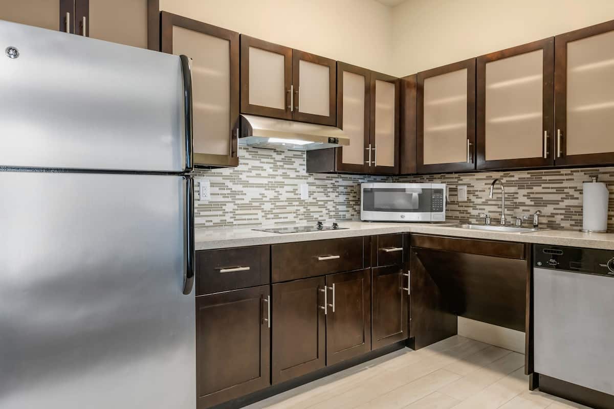 A modern kitchen with stainless steel appliances, dark wooden cabinets, and a tiled backsplash.