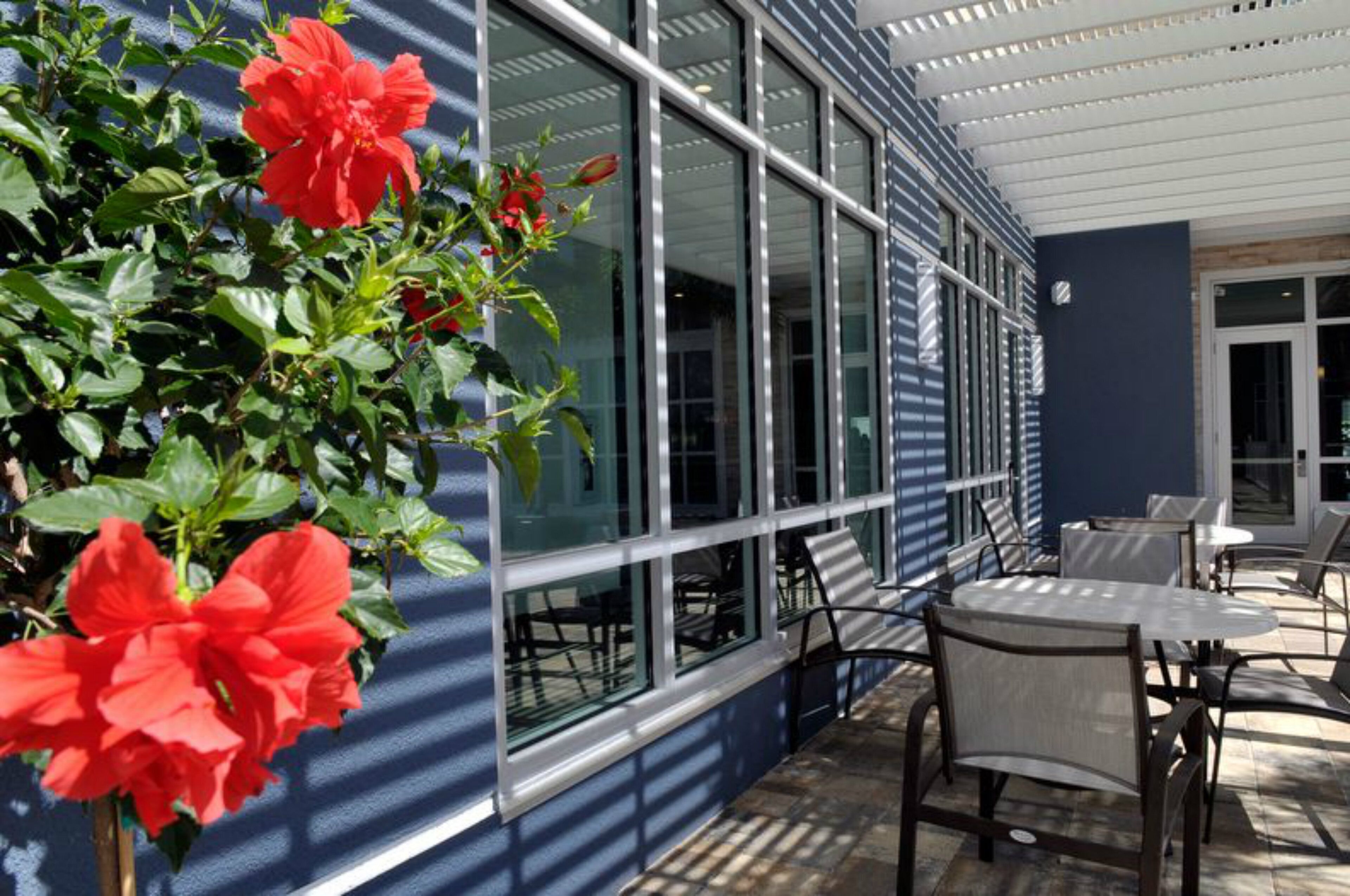 Un patio con mobiliario exterior y un ventanal grande con vistas al interior.