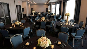 Un salón de conferencias con varias mesas redondas, cada una dispuesta con sillas, velas y centros de mesa florales.