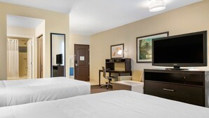 Habitación de hotel con dos camas, un escritorio, una silla, un televisor y una puerta que da a un baño.