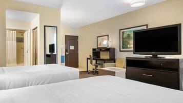 A hotel room with two beds, a desk, a television, and a bathroom.