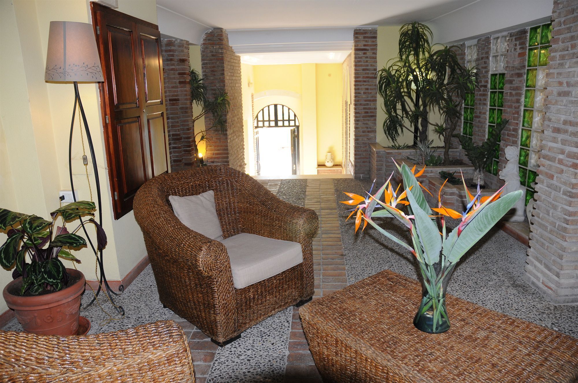 Une pièce avec un fauteuil en osier, un lampadaire et un vase contenant des fleurs de strelitzia.