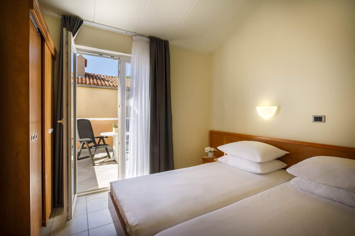 A hotel room with two beds, a nightstand, a lamp, and a view of the outside balcony.