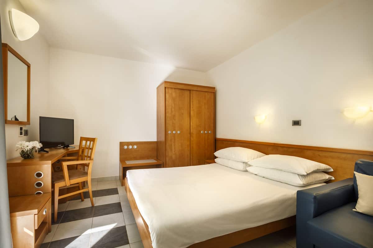 A hotel room with a bed, a desk with a chair, a television, and a wardrobe.