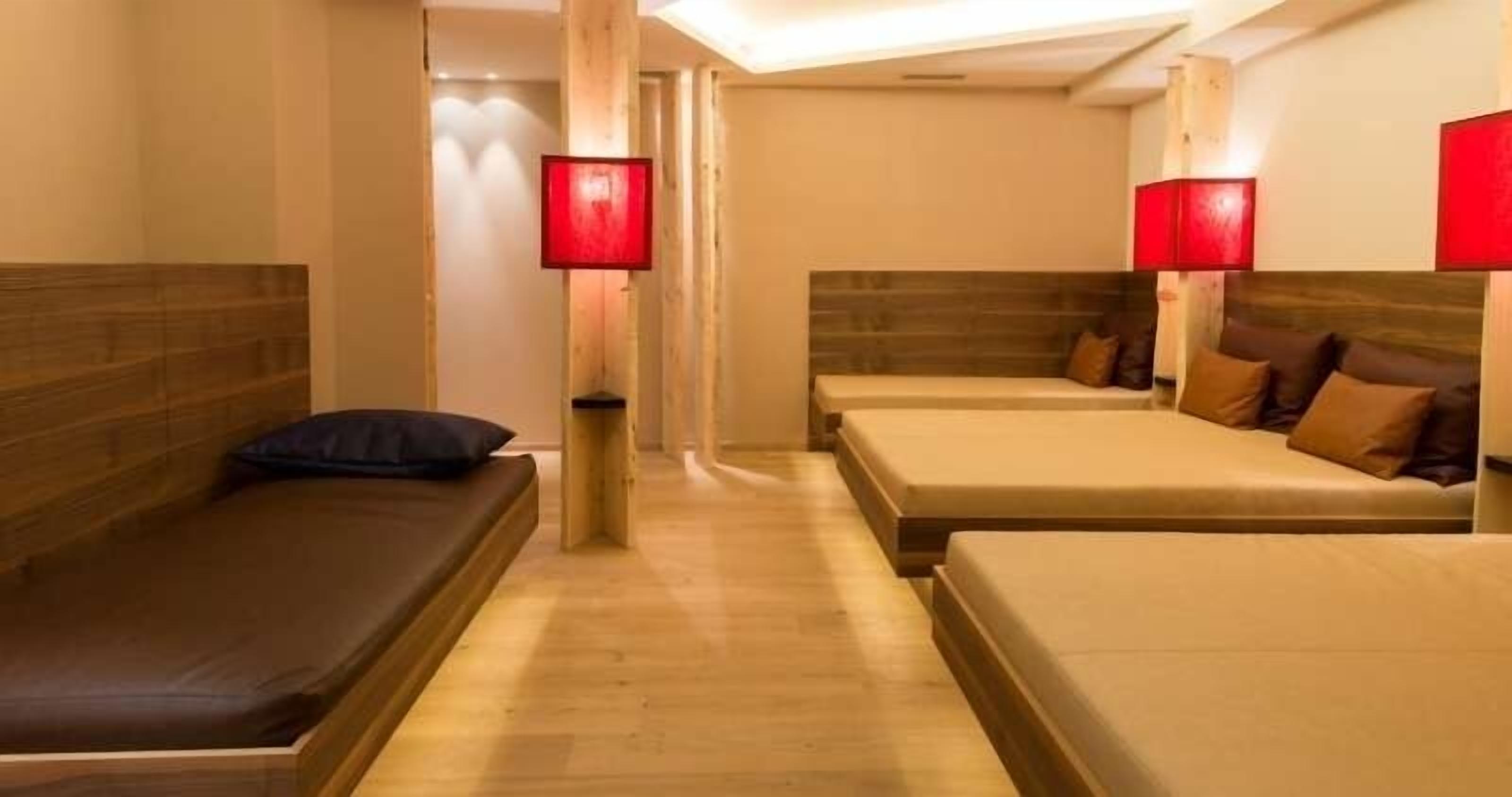 A hotel room with two beds, a wooden floor, and red lamps.