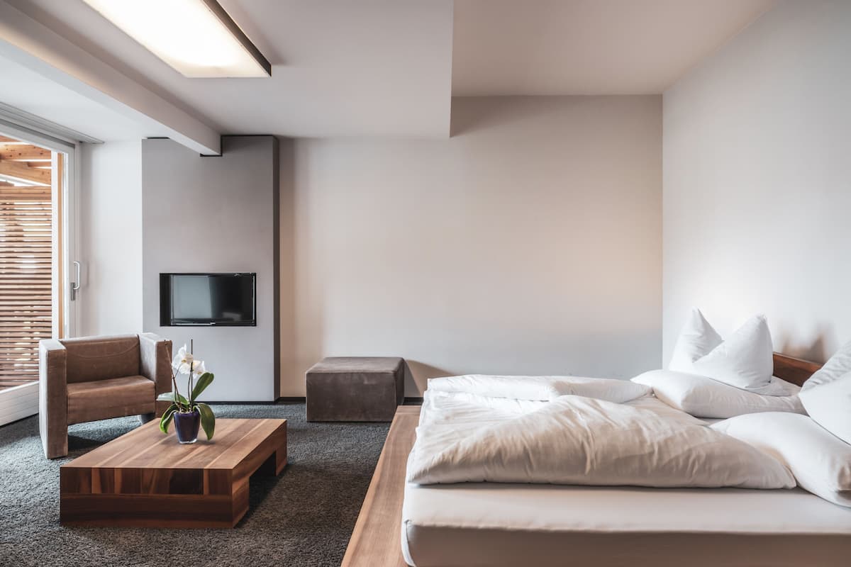 A modern bedroom with a bed, a sofa, a coffee table, and a TV on the wall.