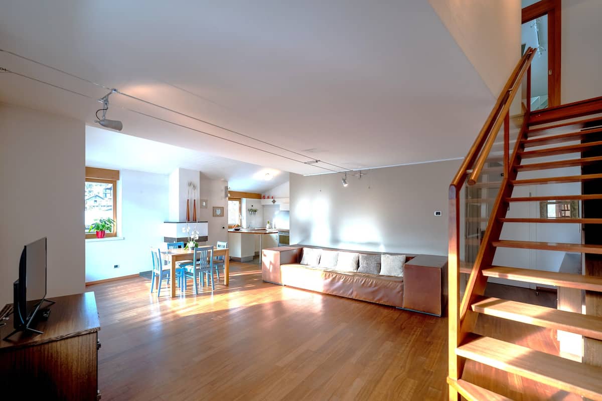 A spacious living area with a wooden floor, a sofa, a dining table with chairs, and a staircase.
