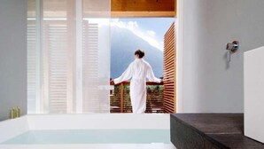 A modern bathroom with a large window, a bathtub, and a wooden ceiling. - Feldmilla Design Hotel – Wellness & SPA (Campo Tures)