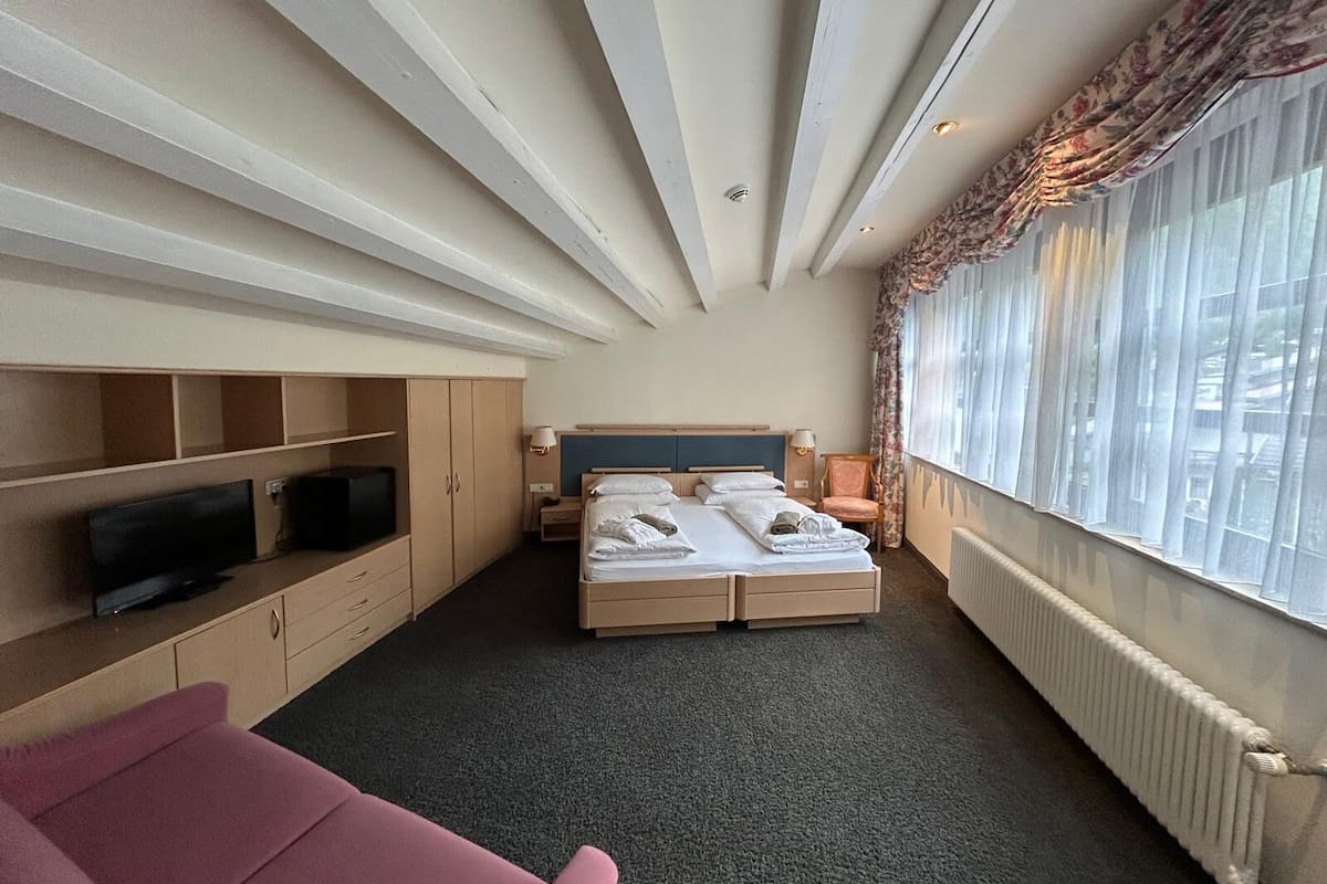A hotel room with a bed, a TV, a desk, and a window with curtains.