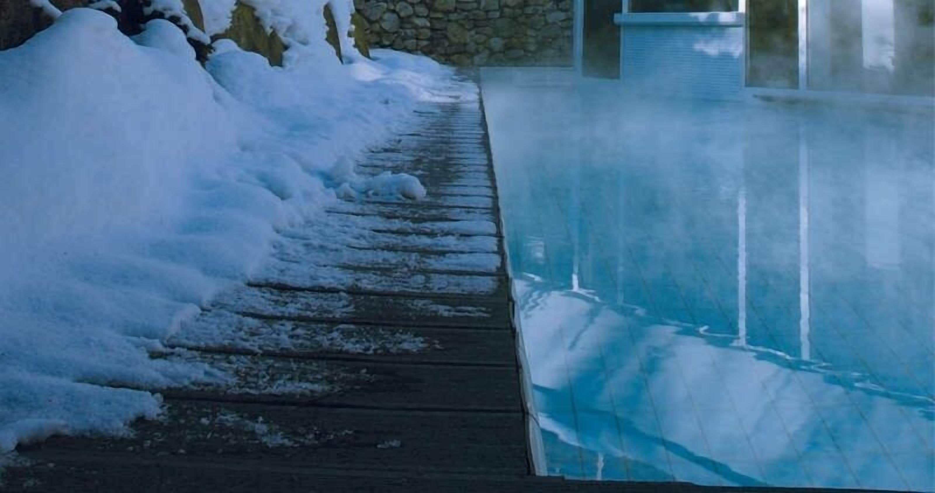 Una terraza de madera que conduce a un jacuzzi rodeado de nieve.