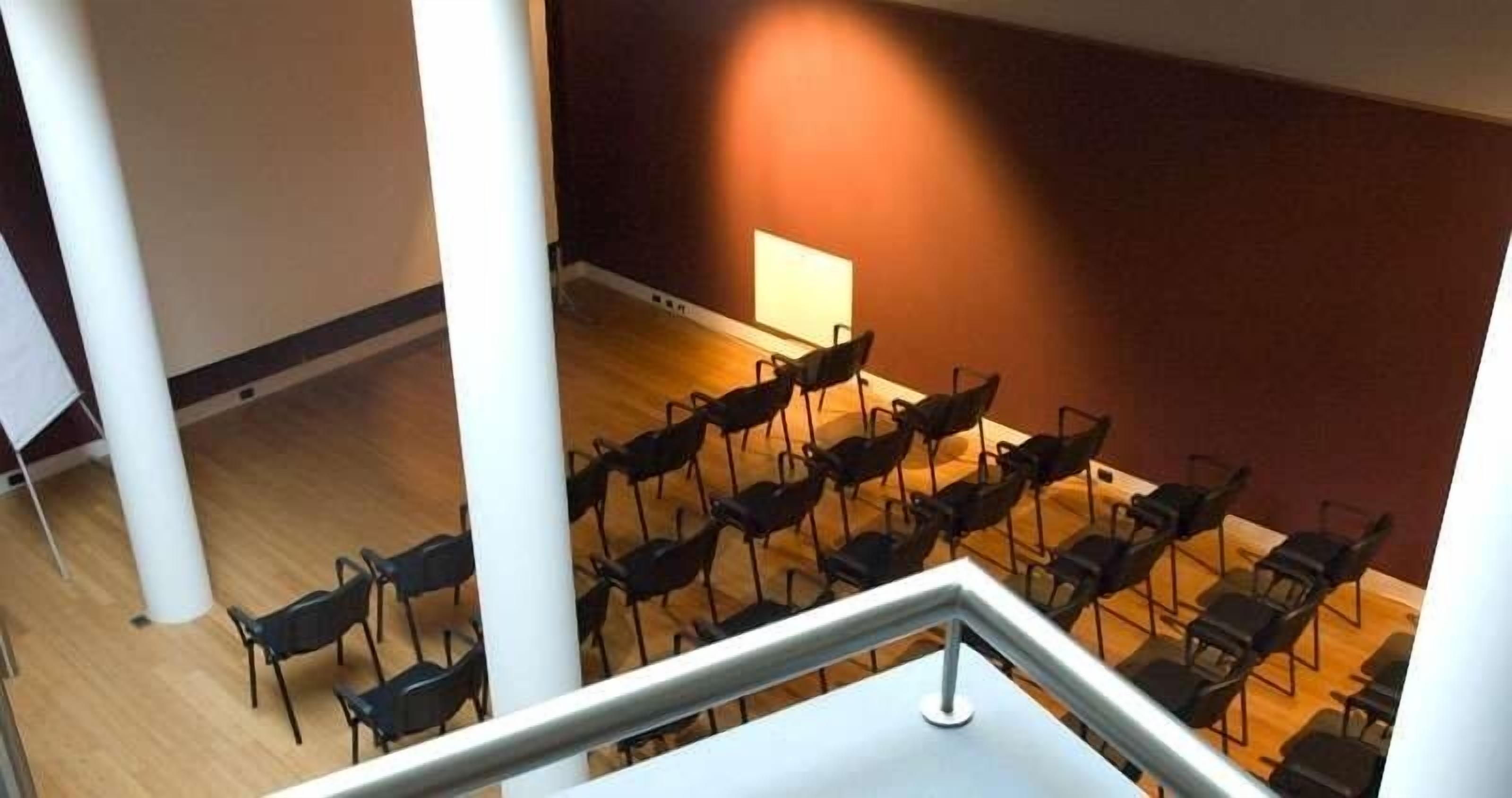 Une salle de conférence avec des rangées de chaises disposées face à un tableau blanc, un plancher en bois et un pilier blanc.