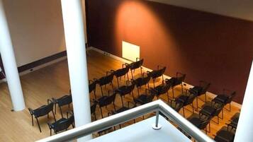 Une salle de conférence avec des rangées de chaises disposées face à un tableau blanc, un plancher en bois et un pilier blanc.