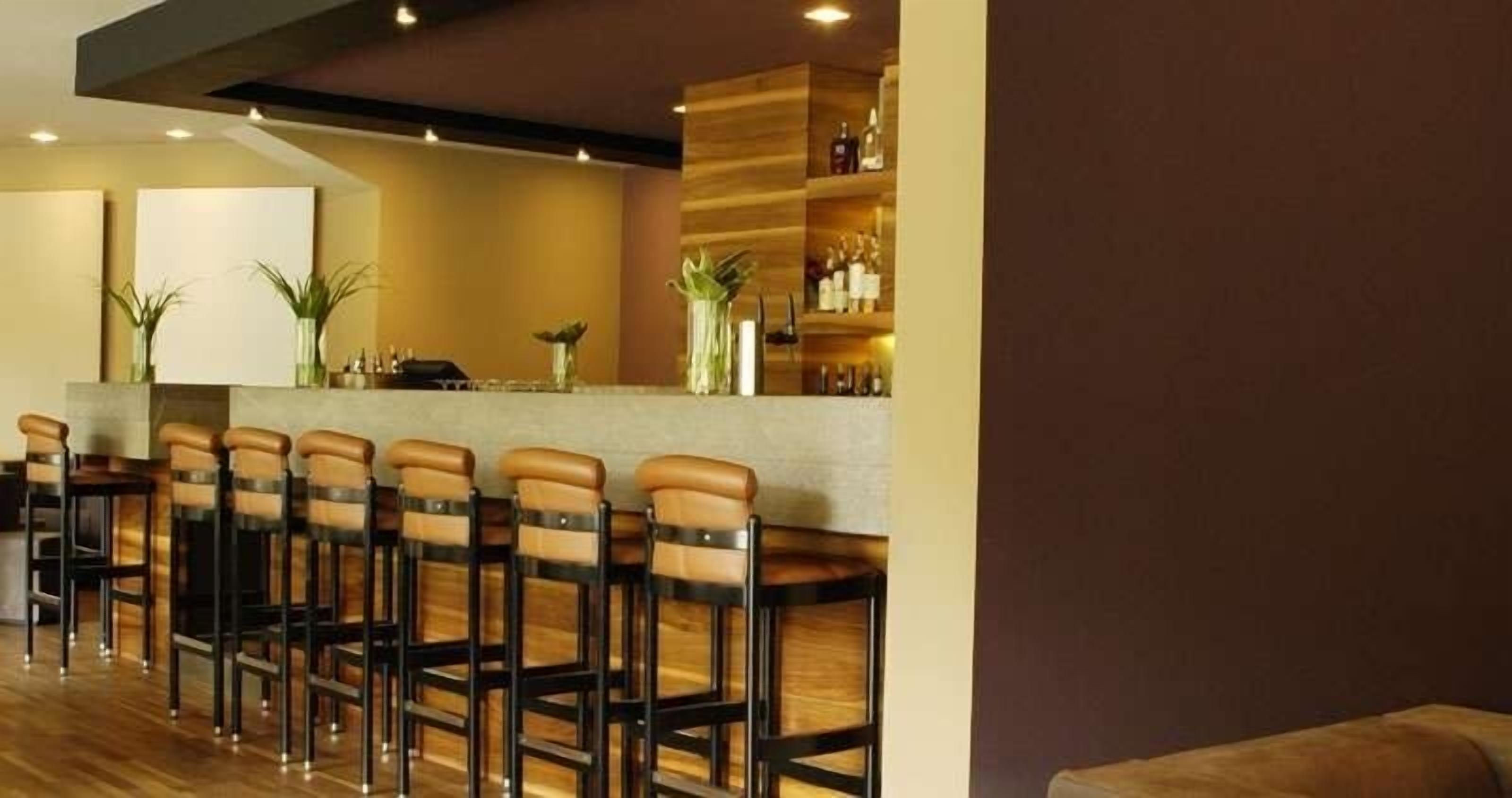Un espace bar avec des tabourets de bar en bois et un comptoir où sont exposées des bouteilles.