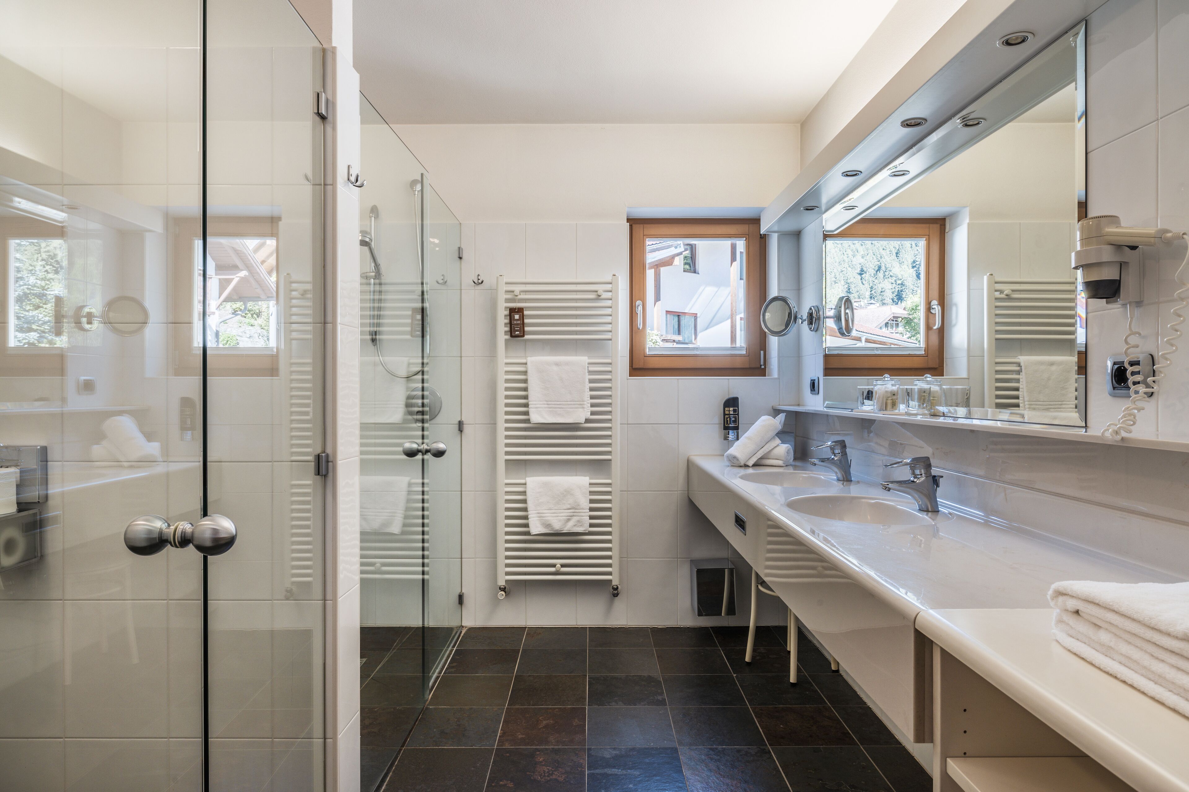 A modern bathroom with a glass shower enclosure, dual sinks, and a large mirror.